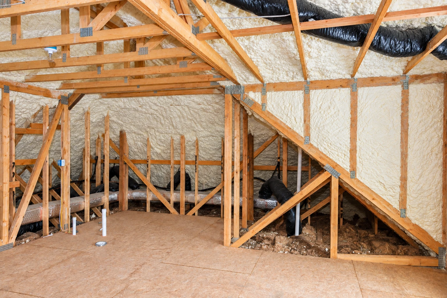 Wood-framed attic with exposed beams and ducts, its roof and walls covered in white spray foam insulation.
