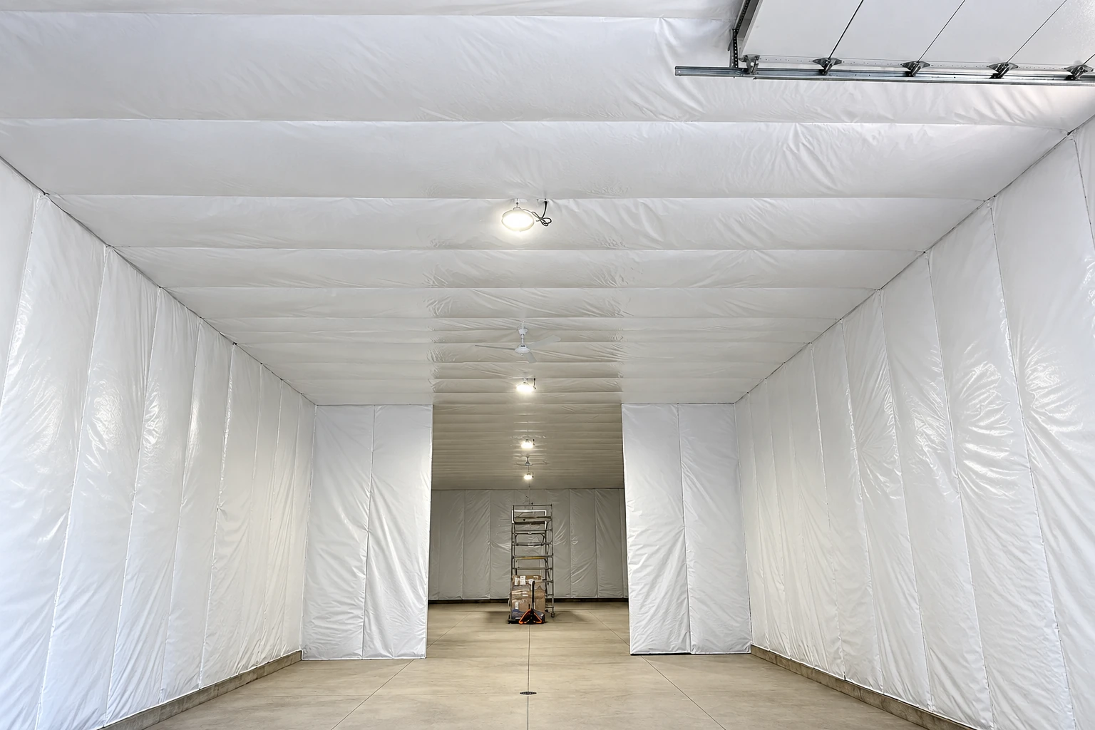 White insulation sheeting covers the walls and ceiling of a large commercial interior, with a ladder at the far end.