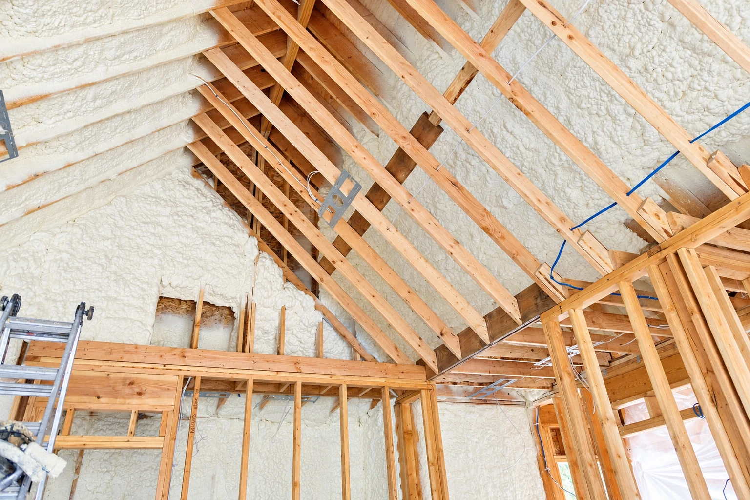 White spray foam insulation coats the roof and walls between exposed wooden rafters in an unfinished attic.