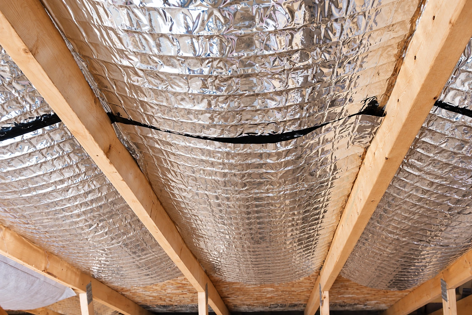 Reflective foil vapor barrier covers the underside of a timber-framed roof.